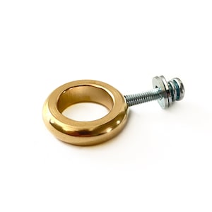 May include: A gold-colored metal ring with a screw and washer attached. The ring is smooth and has a rounded edge.