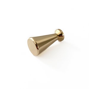 May include: A gold-colored cabinet knob with a conical shape and a flat, rounded base. The knob has a smooth, metallic finish and is designed for furniture hardware. The design is simple and modern, suitable for various interior styles.