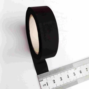 Op de afbeelding: Een rol zwart inktlint voor schrijfmachines met een witte kern, 16 mm. Een liniaal ligt naast het lint en toont metingen in centimeters. Tekst op de afbeelding: 16 mm inktlint, inkribbon, Farbband. Voor schrijfmachine, typewriter, Schreibmaschine.