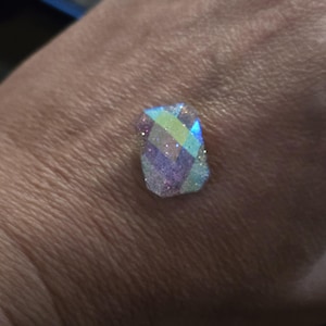 May include: A small, iridescent, multi-faceted gemstone with a light blue, green, and pink hue.