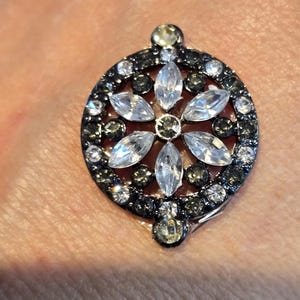 May include: A silver ring with a black and white flower design. The flower is surrounded by smaller black and white stones.