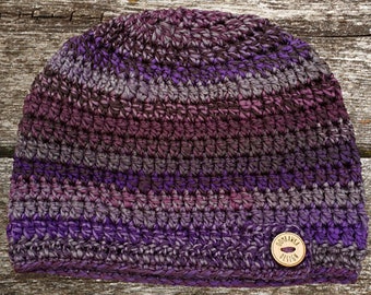 May include: Purple, grey, and brown striped crocheted beanie with a wooden button that says "Goodland Design".