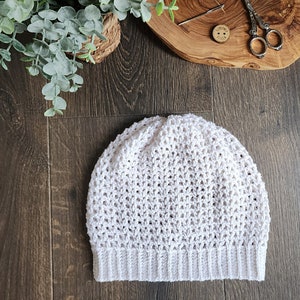 May include: White crocheted beanie hat with a textured stitch pattern. The hat has a folded brim.