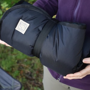 Puede incluir: Una esterilla de dormir negra enrollada con una correa y una etiqueta blanca que dice "Trail Mag"