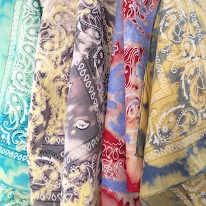 Könnte beinhalten: Vier Bandanas in verschiedenen Farben und Mustern, darunter Blau, Rot, Gelb und Grau. Die Bandanas sind gefaltet und hängen an einer Oberfläche.