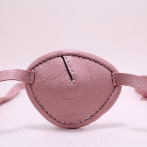 Può includere: Un paraluce per occhio in pelle rosa con un bordo cucito e un cinturino regolabile.