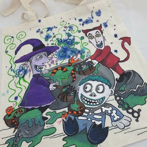 May include: A white canvas tote bag with a hand-painted design featuring characters from the Nightmare Before Christmas. The characters include Sally, Oogie Boogie, and Jack Skellington. The design is colorful and includes green, purple, red, and black.