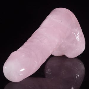 May include: A large, smooth, pink rose quartz carving. The carving is shaped like a human body part.