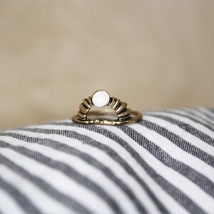 Könnte beinhalten: Ein goldener Ring mit einem weißen Opal-Stein in der Mitte. Der Ring ist in Form eines Halbmondes geformt.