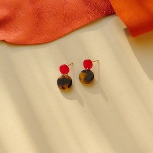 Könnte beinhalten: Ein Paar Ohrringe mit einem Schildpattmuster-Scheibe und einem kleinen roten Akzent.