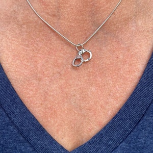 May include: A silver chain necklace with a charm of two linked handcuffs.