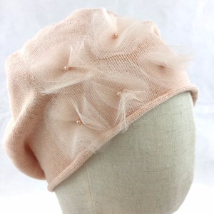 Puede incluir: Un gorro de punto rosa pálido con una delicada superposición de tul y adornos de perlas.