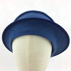 May include: A blue cloche hat with a dark blue ribbon trim. The hat is made of a soft, felt-like material and has a rounded crown and a wide brim. The hat is displayed on a mannequin head against a white background.