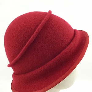 May include: A cloche hat in a deep red hue. The hat features a rounded crown with a decorative band and a slightly turned-up brim. The brim is trimmed with a matching red ribbon, offering a classic and elegant look.