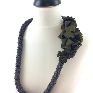 May include: A gray and green fabric necklace with a large green fabric flower accent. The necklace is made of multiple layers of fabric that have been twisted and knotted together.