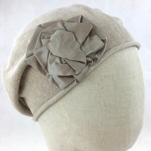 May include: A beige knitted beret with a large, beige fabric flower accent.