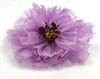 May include: A large, purple, fabric flower with a ruffled texture. The center of the flower has a dark brown and yellow center.