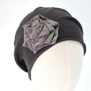 May include: A grey knit beanie with a large grey fabric rose on the side.