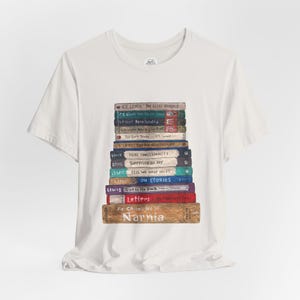 May include: White t-shirt featuring a stack of books with titles by C.S. Lewis, including "The Chronicles of Narnia" and "Mere Christianity." The books are in various colors, with the titles clearly visible. The shirt is made of a soft material.