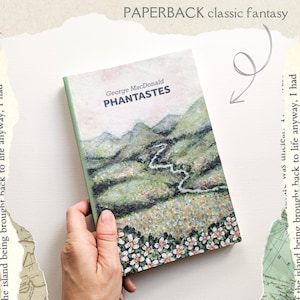 May include: A paperback book with a green, white, and brown cover featuring a landscape scene with a winding river. The title of the book is "Phantastes" by George MacDonald. The book is labeled as a "classic fantasy" paperback.