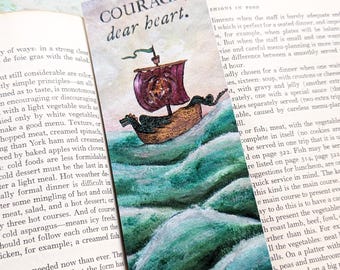May include: A watercolour illustration of a ship sailing on a turquoise sea. The ship has a red sail with a gold design and a brown hull. The text "COURAGE, dear heart." is written in black lettering on a white background.