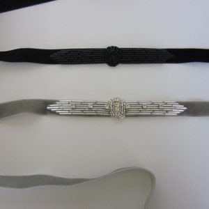 May include: Two chokers: one black, one gray. The black choker features a black beaded centerpiece. The gray choker has a silver-toned centerpiece with clear crystals. Both chokers have a velvet band.