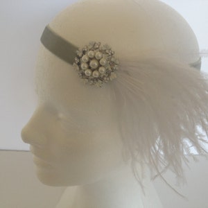 May include: A grey headband featuring a circular embellishment composed of white faux pearls and clear crystals. A cluster of long, wispy white feathers is attached to the side of the headband, extending outward from the central decorative piece.