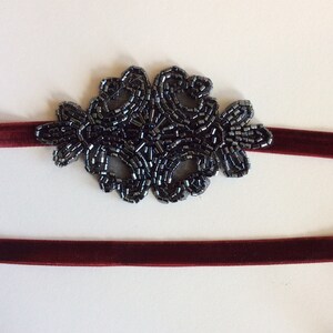 Peut inclure: Un bandeau en velours bordeaux orn&eacute; d'une d&eacute;coration florale en perles gris fonc&eacute;. La d&eacute;coration perl&eacute;e est centr&eacute;e sur le bandeau, cr&eacute;ant un accent d&eacute;coratif. Un accessoire simple et &eacute;l&eacute;gant.