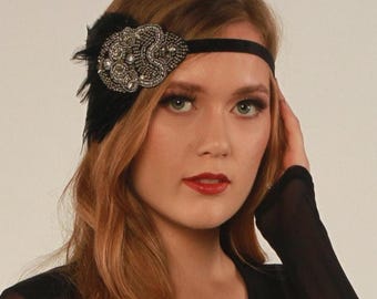 May include: Black flapper-style headband with a central beaded embellishment and black feathers. The beaded section features silver and clear beads in an oval shape. The headband is made of a black, velvet-like material, suitable for special occasions.