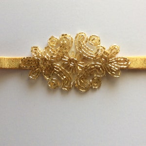 Peut inclure: Un bandeau dor&eacute; avec un motif floral en perles. Le bandeau &eacute;lastique est de couleur or. Le motif floral est compos&eacute; de petites perles dor&eacute;es, cr&eacute;ant un motif d&eacute;licat. Accessoire de cheveux.