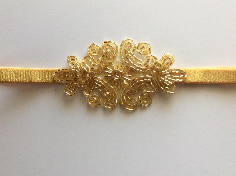 Peut inclure: Un bandeau dor&eacute; avec un motif floral en perles. Le bandeau &eacute;lastique est de couleur or. Le motif floral est compos&eacute; de petites perles dor&eacute;es, cr&eacute;ant un motif d&eacute;licat. Accessoire de cheveux.