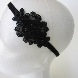 Peut inclure: Bandeau noir orn&eacute; de perles. Il pr&eacute;sente un grand motif floral sur le c&ocirc;t&eacute;, compos&eacute; de petites perles sombres, cr&eacute;ant un aspect textur&eacute; et d&eacute;taill&eacute;. Le bandeau est pr&eacute;sent&eacute; sur une t&ecirc;te de mannequin blanche.