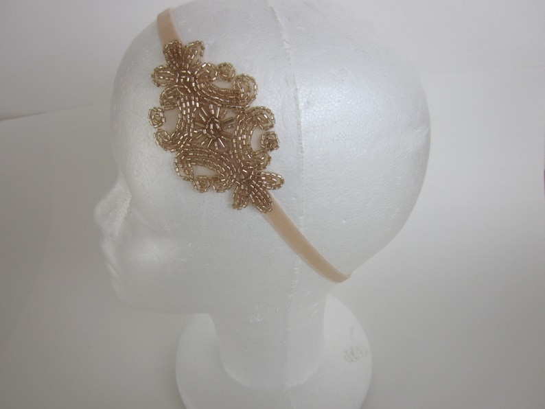 Peut inclure: Un bandeau dor&eacute; orn&eacute; de perles avec un motif floral. Le bandeau est compos&eacute; d'un ruban en velours beige doux et d'un groupe de perles dor&eacute;es dispos&eacute;es en motif d&eacute;coratif. L'ornement perl&eacute; mesure environ 7.6 cm de large.