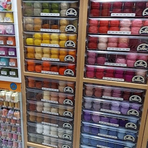 May include: A wall of drawers filled with colorful spools of DMC embroidery floss. Each drawer is labeled with a DMC color number.