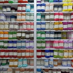 May include: A wall of shelves filled with colourful yarn balls, each labelled with a number. The yarn is organised by colour and number, creating a visually appealing display.
