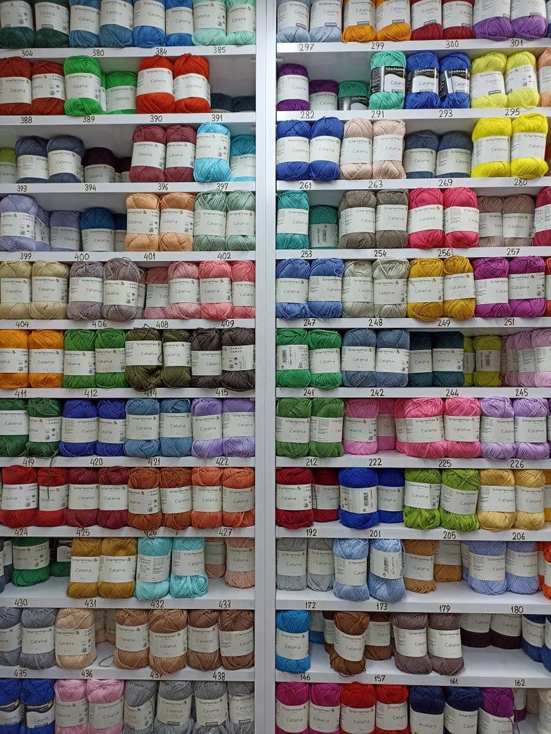 May include: A wall of shelves filled with colourful yarn balls, each labelled with a number. The yarn is organised by colour and number, creating a visually appealing display.