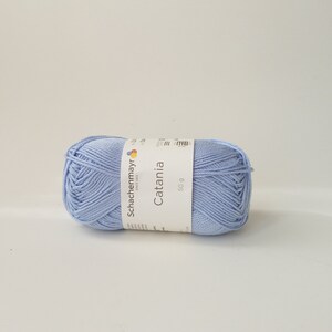 May include: A ball of light blue Catania yarn by Schachenmayr, a German yarn company, with a label that says "Catania" and "50 g".