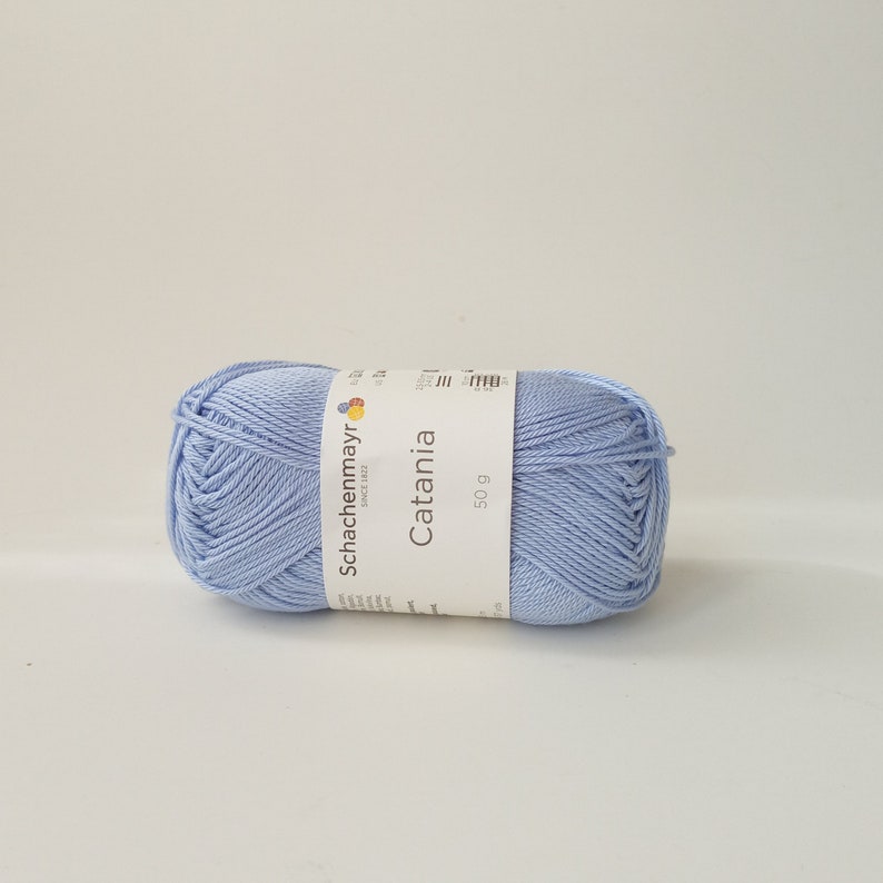 May include: A ball of light blue Catania yarn by Schachenmayr, a German yarn company, with a label that says "Catania" and "50 g".