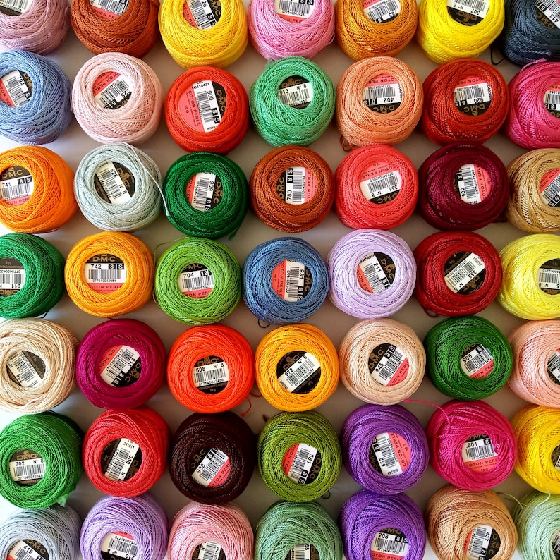 May include: A collection of colorful embroidery floss spools with DMC branding. The spools are arranged in a grid pattern on a white surface.