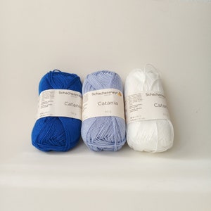 May include: Three balls of yarn in blue, light blue, and white. Each ball has a label that says "Schachenmayr Catania" and "50 g".