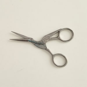 Pode incluir: Tesoura decorativa prateada com um design de pássaro. A tesoura tem duas alças circulares.