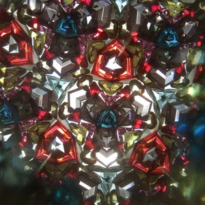 May include: A kaleidoscope image with a symmetrical pattern of red, blue, green, and gold geometric shapes.