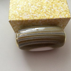 May include: A gold and white striped bottle stopper with a gold rim. The stopper has a white center and is made of glass.