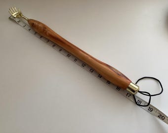 May include: A wooden back scratcher with a gold metal hand at the top and a gold metal tip at the bottom. The scratcher is about 18 inches long and has a black elastic band attached to the bottom.