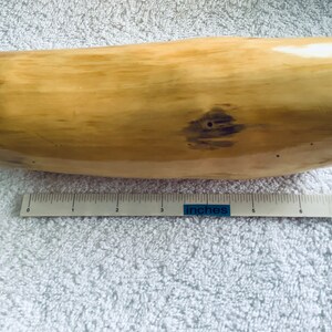 May include: A light brown, smooth, cylindrical piece of wood with a dark brown knot. The wood is approximately 17.8 cm long.