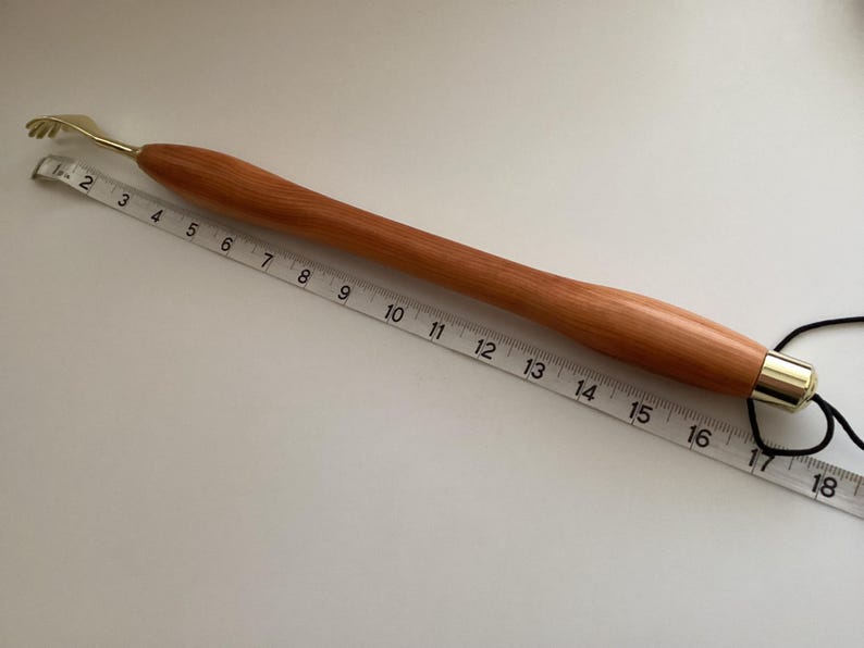 May include: A wooden back scratcher with a brass tip and a black cord. The scratcher is 43 cm long.