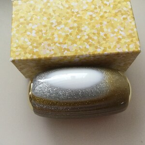 May include: A gold and silver glitter oval-shaped container with a white center.