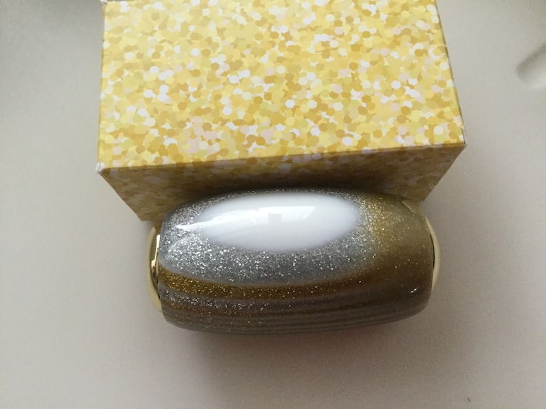 May include: A gold and silver glitter oval-shaped container with a white center.