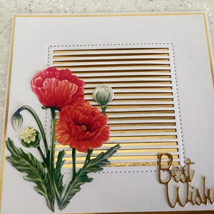 May include: A white greeting card with a gold border and accents. The card features a floral design with red poppies and green leaves. The words "Best Wishes" are in gold script.