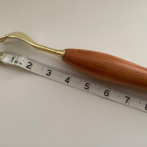 May include: A wooden handled back scratcher with a gold metal hook. The scratcher is 15 cm long and is measured against a tape measure.